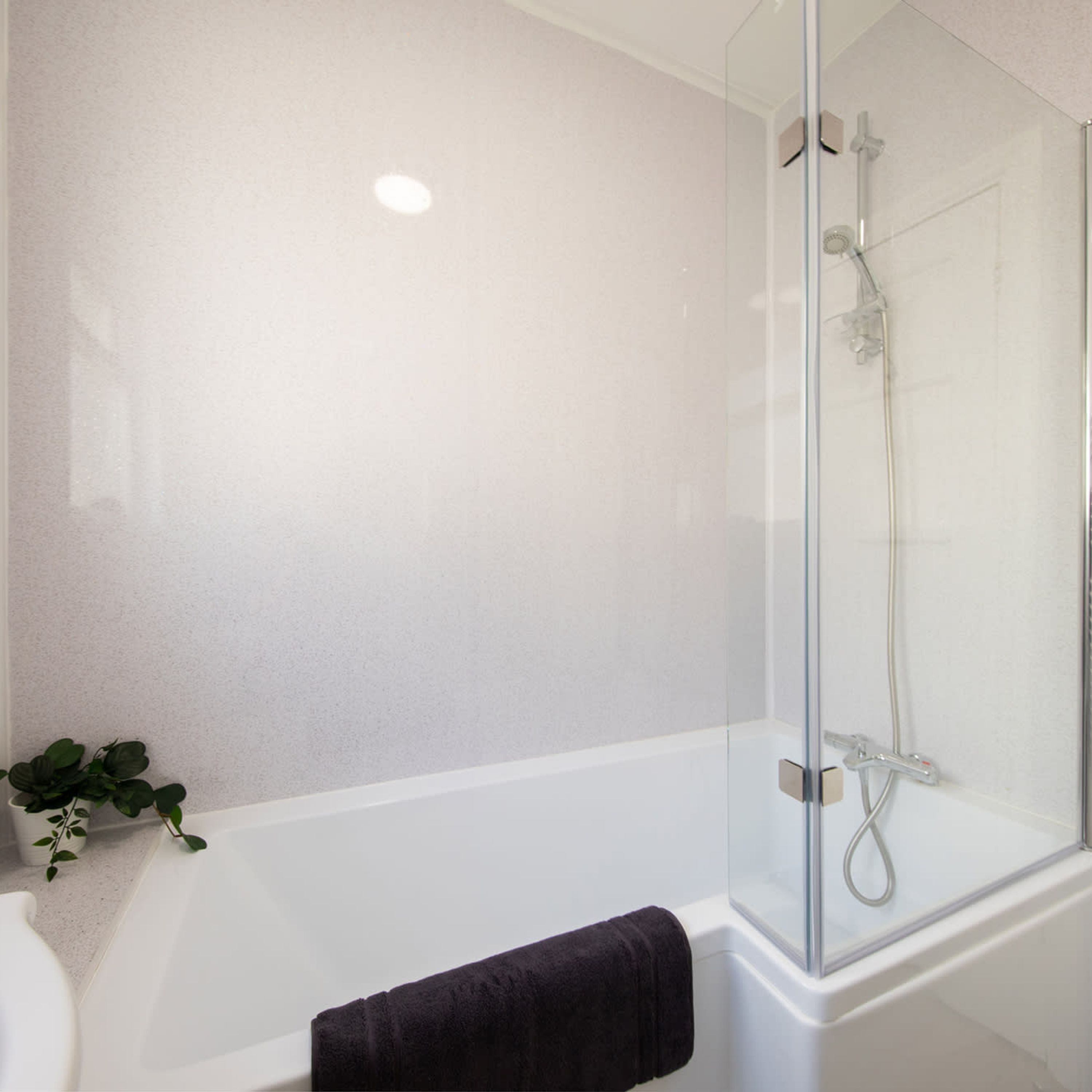 A modern bathroom with a glass-enclosed shower, a white bathtub, and a potted plant.