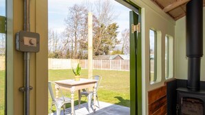 A room with a wooden stove, a table with chairs, and a view of a grassy yard. - Unique Comfy Remodelled Railway Carriage (Chichester)