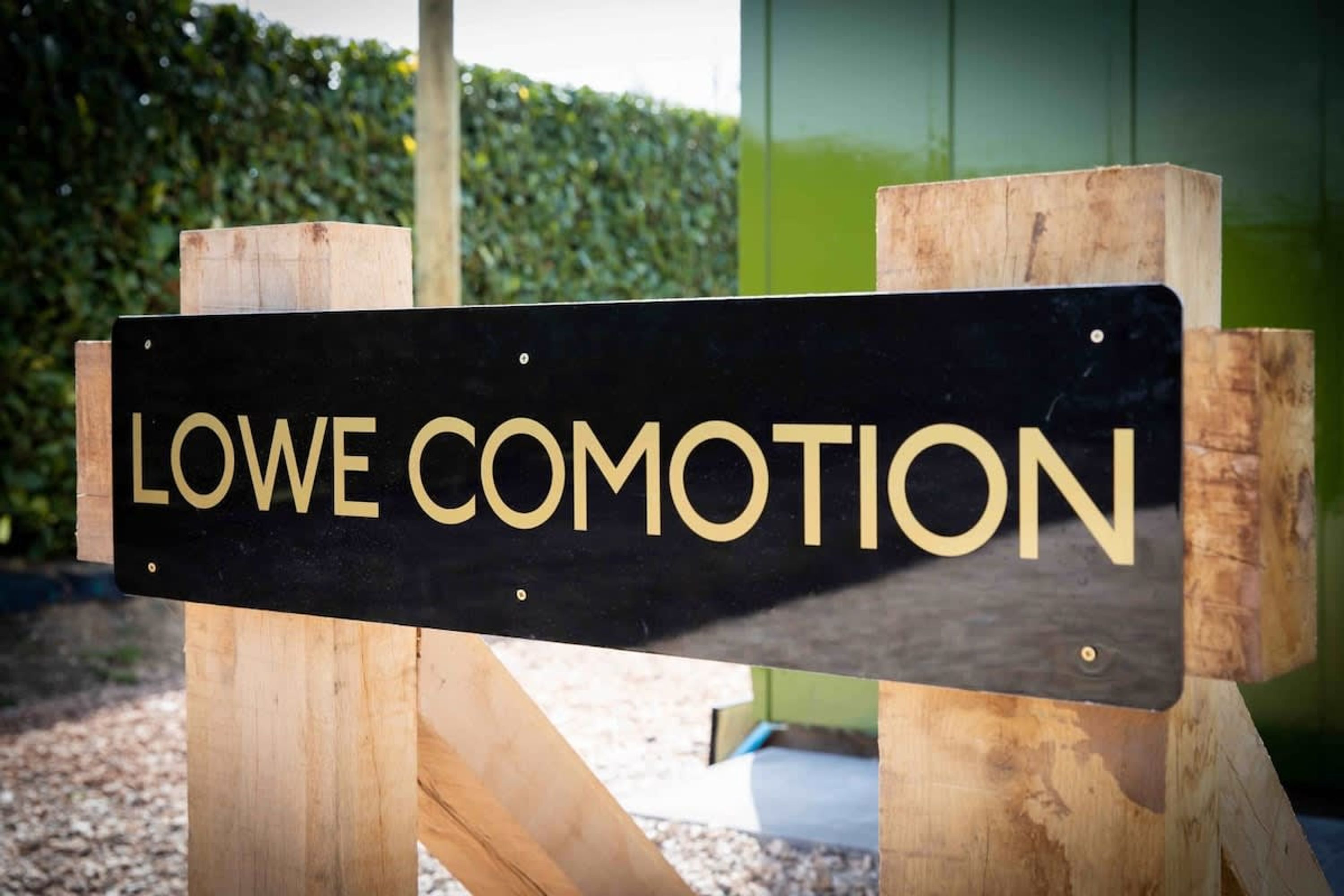 A sign with the text "LOWE COMOTION" mounted on a wooden post.