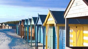 A row of beach huts with a sandy beach and clear sky in the background.