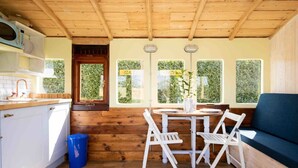 A compact kitchen with white cabinets, a wooden ceiling, and a window with a view of greenery. - Unique Comfy Remodelled Railway Carriage (Chichester)