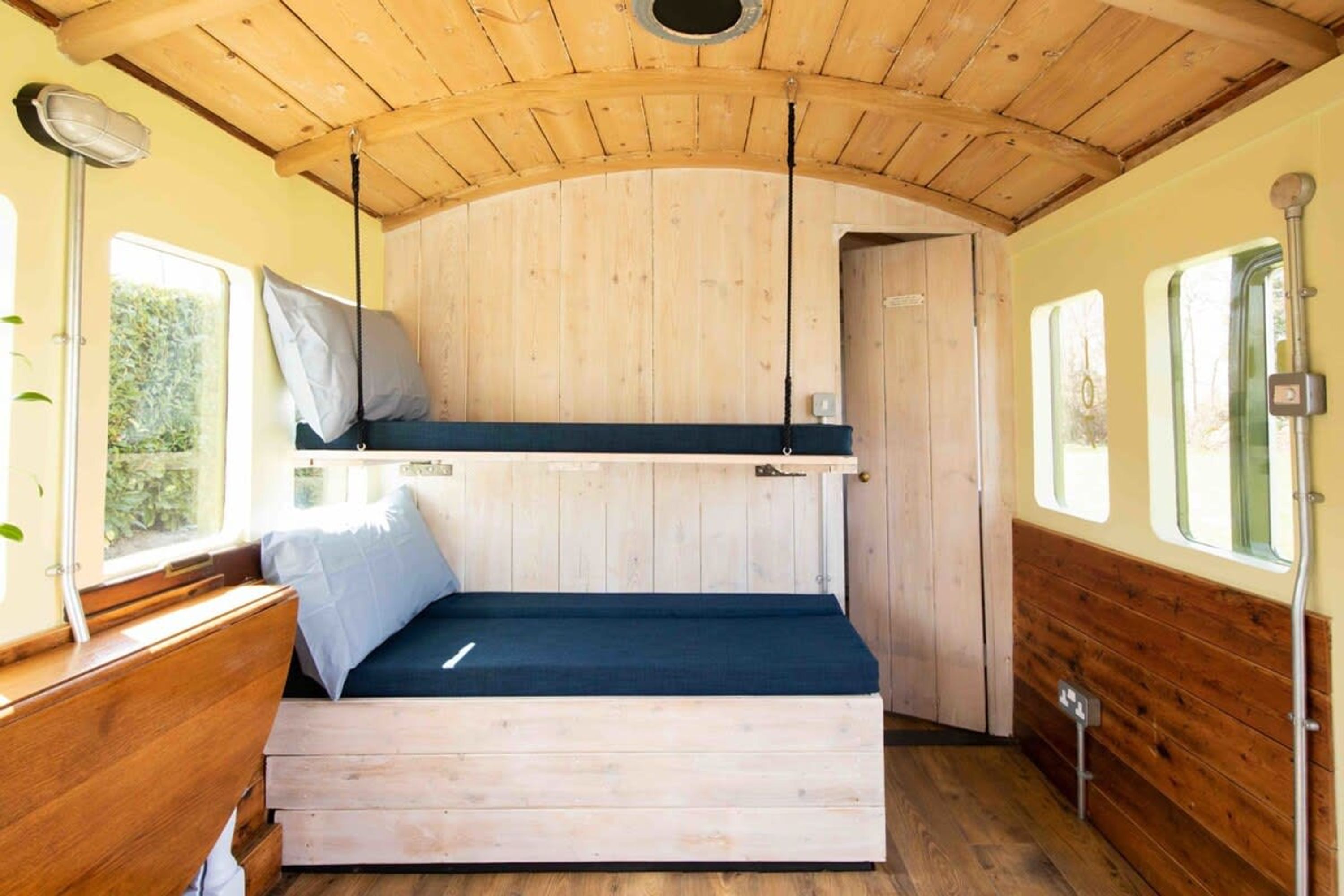 A compact, wooden interior with a bunk bed, a small table, and a bench.