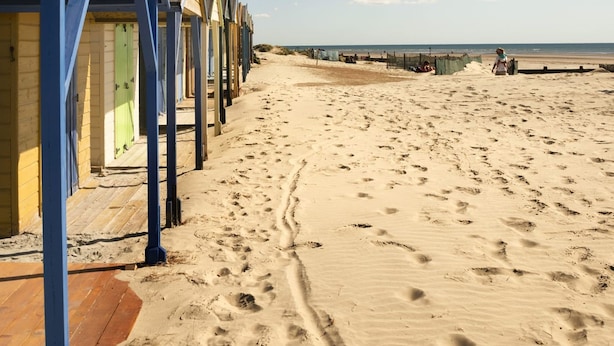 A row of beach huts with a sandy beach and the sea in the background.