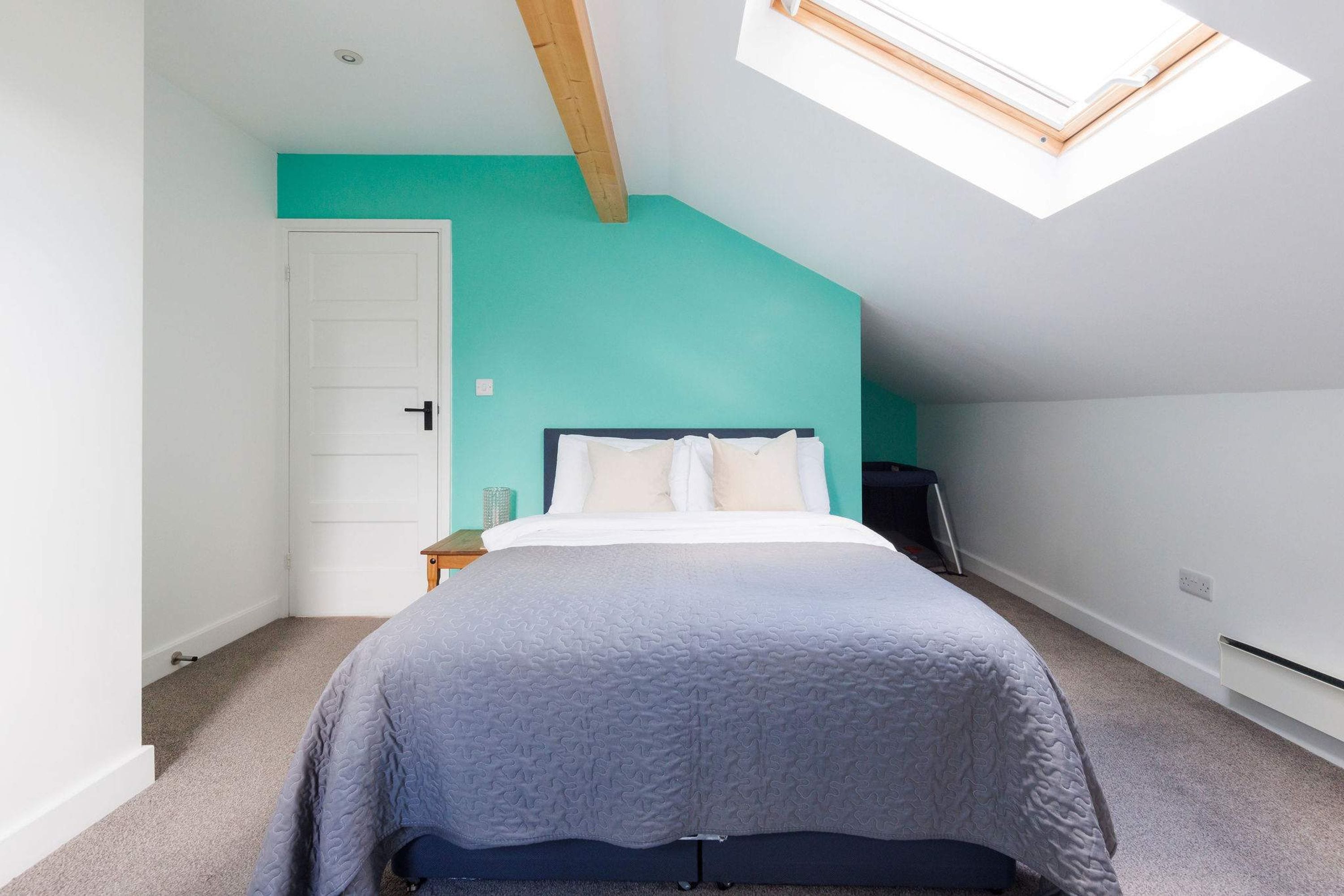A bedroom with a sloped ceiling, a skylight, a bed with a headboard, a nightstand, and a wall with a teal accent.