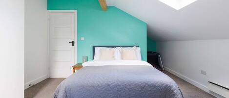 A bedroom with a sloped ceiling, a skylight, a bed with a headboard, a nightstand, and a wall with a teal accent.