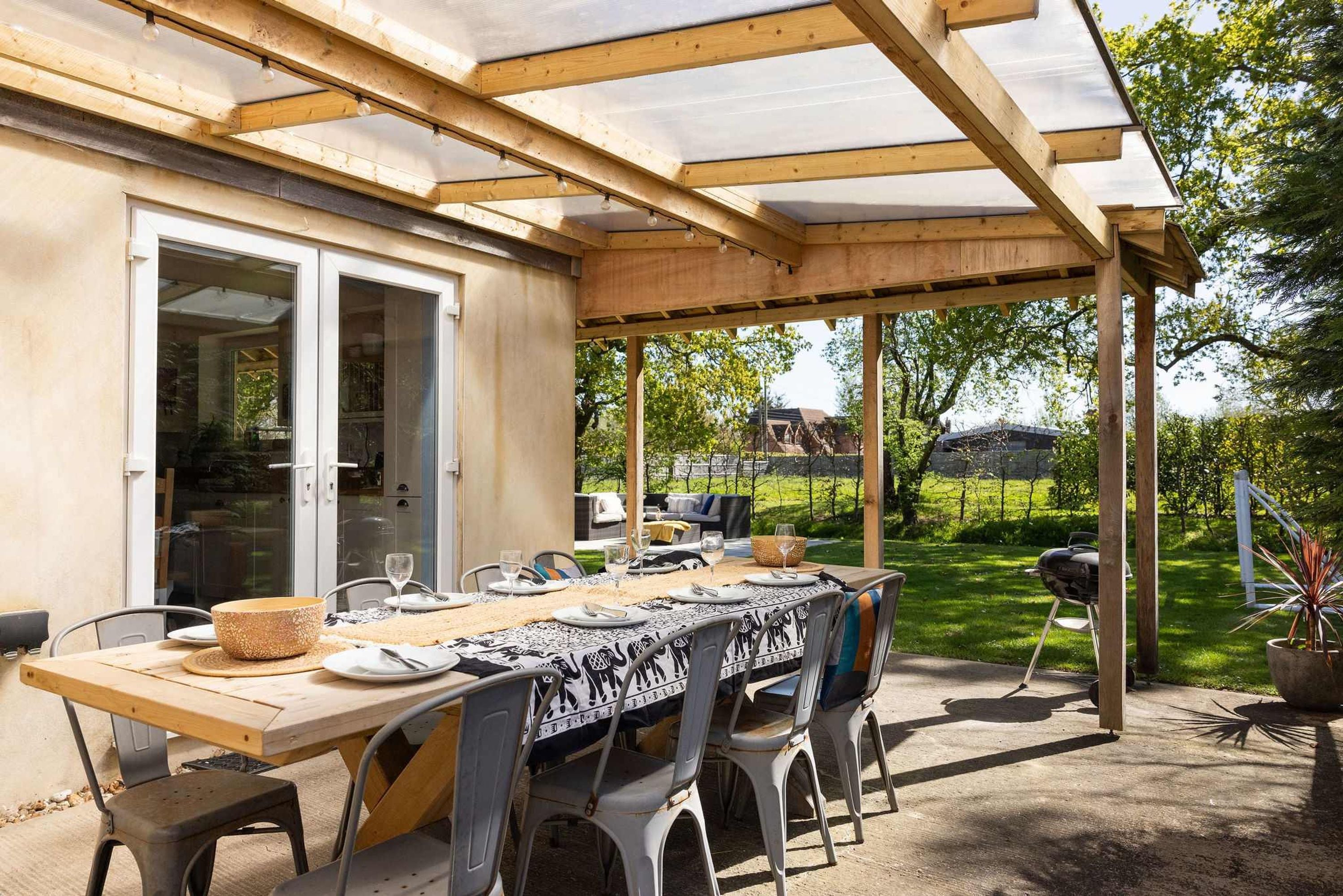 An outdoor patio with a wooden table set for dining, surrounded by chairs.
