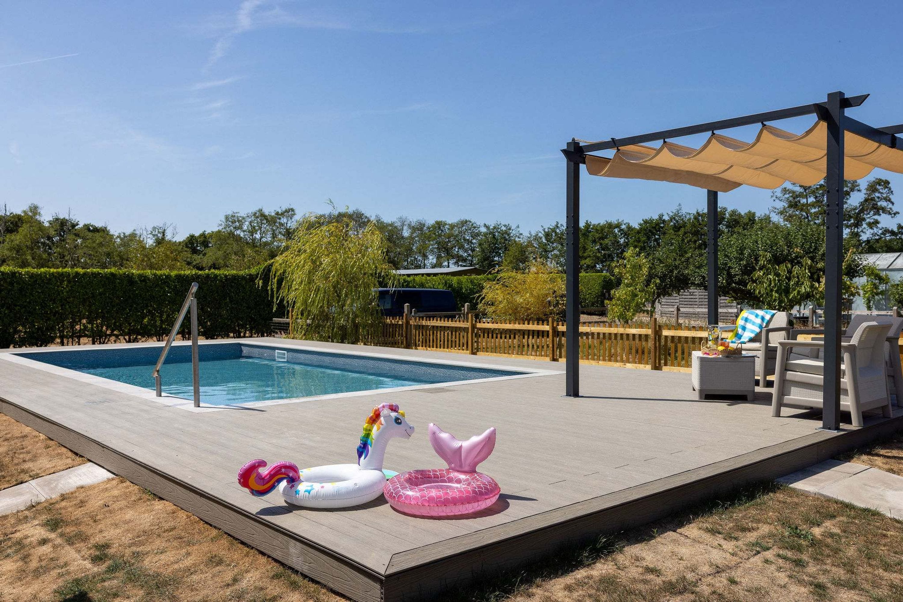 A swimming pool with a wooden deck, a covered seating area, and inflatable toys.