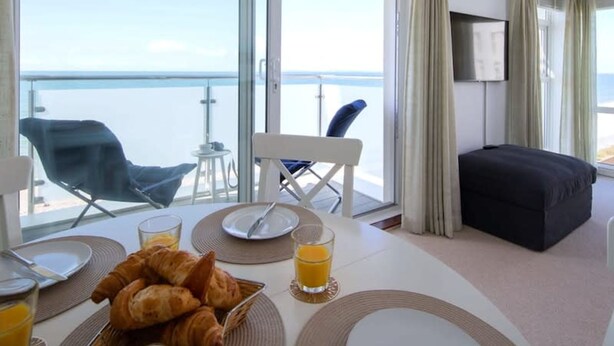 A balcony with a table set for breakfast, including croissants and orange juice, overlooking a body of water.