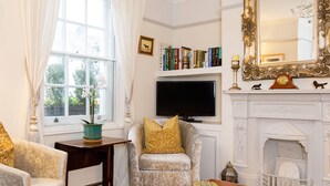 A living room with a fireplace, a television, and a bookshelf. - Beautiful Georgian Home in the Heart of Chichester (Chichester)