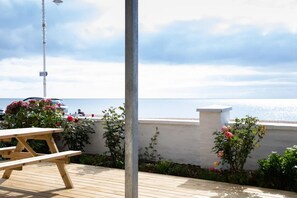 A wooden deck with a picnic table, a metal pole, and a white wall with a railing.