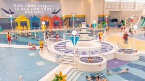 An indoor swimming pool with multiple lanes, a central water feature, and colorful play structures. - Absolute Beachfront With Decked Garden Oasis and Views (Bognor Regis)