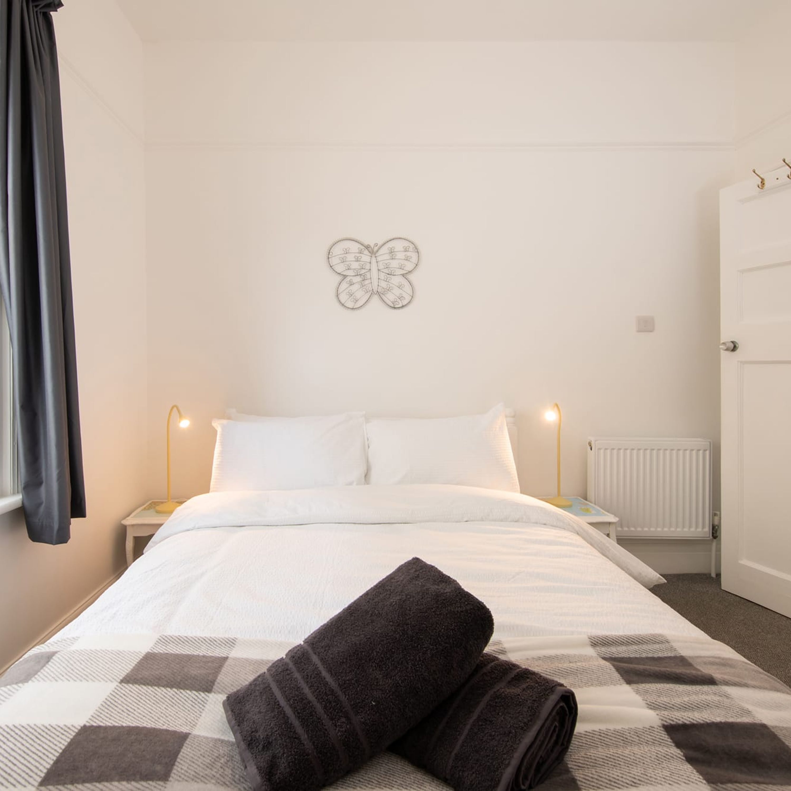 A neatly made bed with white linens, a dark brown towel, and a wall-mounted butterfly art piece.