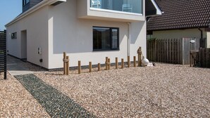 Uma casa moderna de dois andares com varanda, cerca de madeira e entrada com calçamento de brita.
