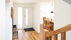 Interior moderno com escada de madeira, área de jantar com cadeiras de madeira e uma porta que dá para outro cômodo.