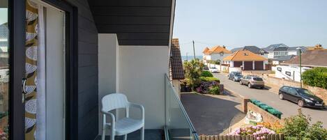 A balcony with a white plastic chair, a view of a residential street, and a clear sky.