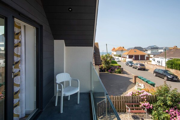 A balcony with a white plastic chair, a view of a residential street, and a clear sky.