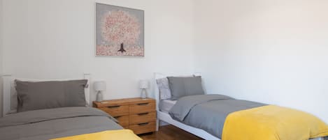 Un dormitorio con dos camas, una mesita de noche de madera, una mesilla auxiliar y un cuadro colgado en la pared.