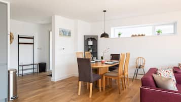 A modern living space with a dining area, a sofa, and a window with plants.