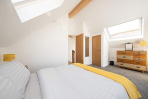 A bedroom with a bed, a dresser, a mirror, and a skylight.