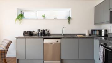 A modern kitchen with grey cabinetry, a dishwasher, a coffee maker, and a microwave.
