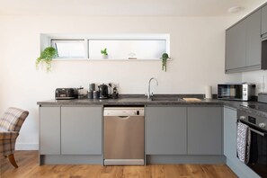 A modern kitchen with grey cabinetry, a dishwasher, a coffee maker, and a microwave.