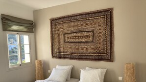 A bedroom with a large bed, two pillows, a woven tapestry on the wall, and a window with curtains.
