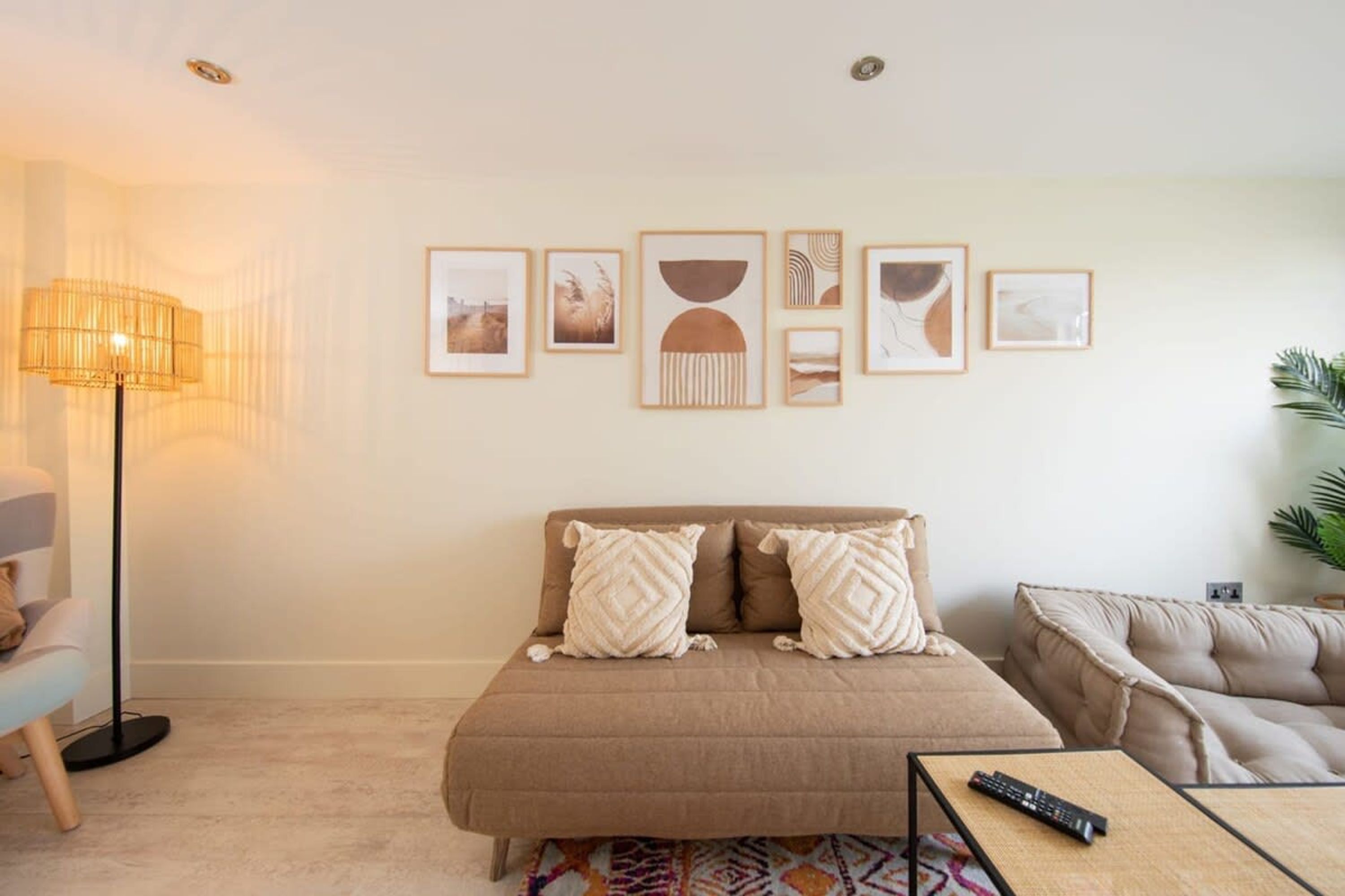 A bedroom with a bed, a sofa, a floor lamp, and a wall with framed pictures.