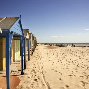A row of beach huts with a sandy beach and the sea in the background. - Designer Family Escape Hot Tub Steps to Beach (Chichester)