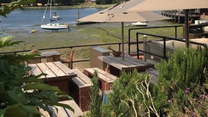 Eine Uferterrasse mit Holzmöbeln, ein Boot liegt im Wasser, und ein großer Sonnenschirm spendet Schatten.