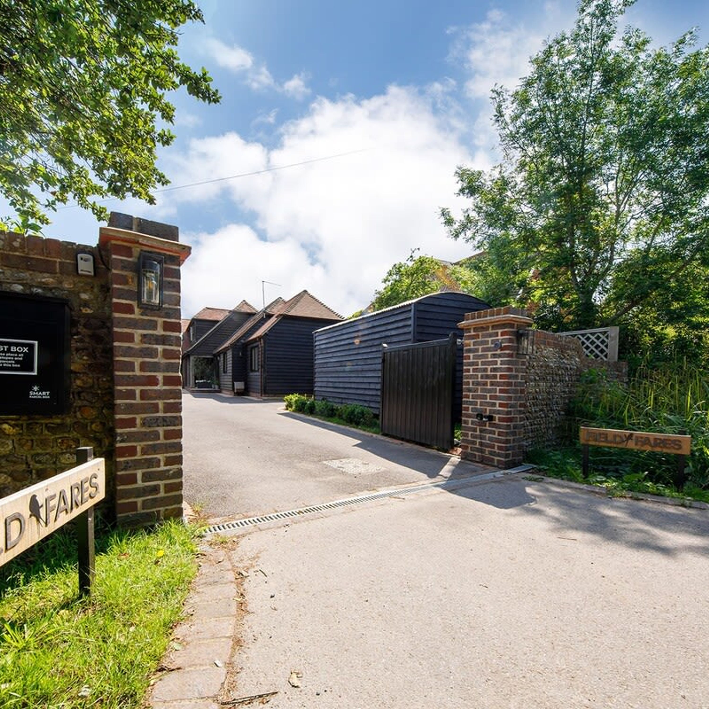 A gated residential area with a brick wall and a metal gate. There is a sign on the wall that reads "D FARES" and another sign on the gate that reads "FIELDY FARES".