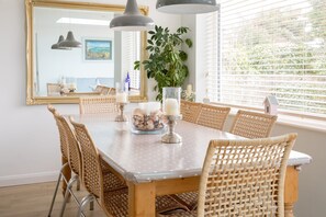 A dining area with a round table, wicker chairs, a vase with flowers, and a large mirror on the wall. - Tranquil Family Retreat 5 min to Beach Garden (Chichester)