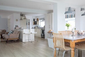 A modern kitchen with white cabinets, a dining area with a wooden table and wicker chairs, and a living room with a sofa and a coffee table. - Tranquil Family Retreat 5 min to Beach Garden (Chichester)