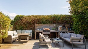 An outdoor patio with a wooden deck, a built-in grill, and a seating area with sofas and chairs. - Tranquil Family Retreat 5 min to Beach Garden (Chichester)