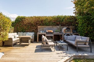 Un patio exterior con terraza de madera, una parrilla empotrada y una zona de estar con sofás y sillones.