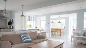 A spacious living area with a beige sofa, a wooden coffee table, and a dining area with a table and chairs. - Tranquil Family Retreat 5 min to Beach Garden (Chichester)