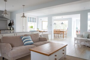 Un amplio salón con un sofá color beige, una mesa de centro de madera y una zona de comedor con mesa y sillas.