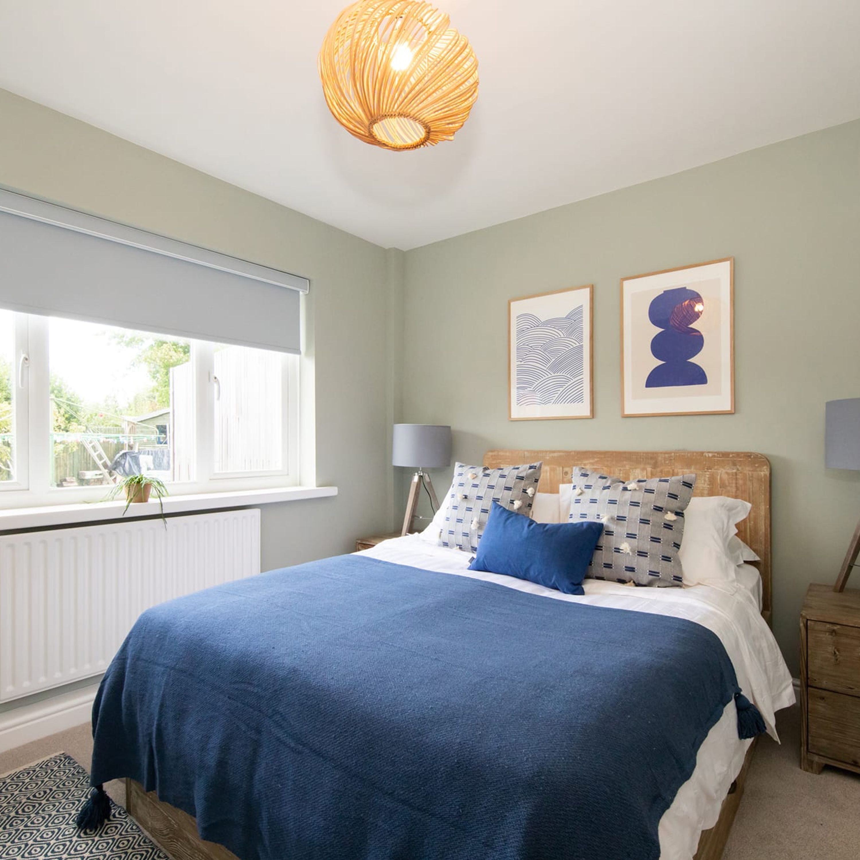 A bedroom with a bed, a window, a radiator, and two wall-mounted lamps.