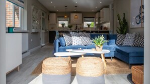 A modern living room with a blue sofa, geometric pillows, a white coffee table, and woven ottomans. - Bosham 3 BR Beach House With Garden Playhouse (Chichester)
