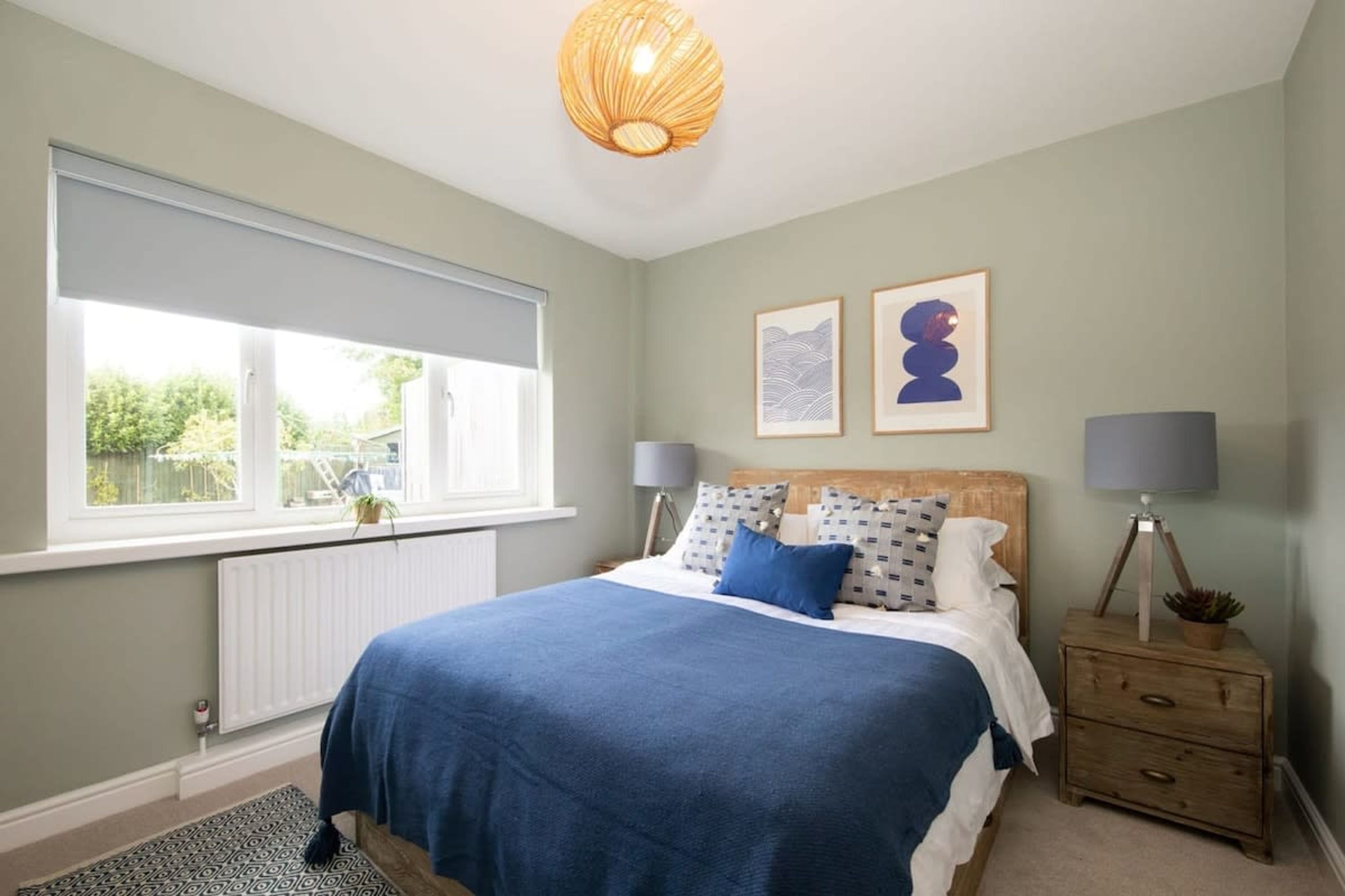 A bedroom with a bed, bedside tables, a window with blinds, and artwork on the wall.