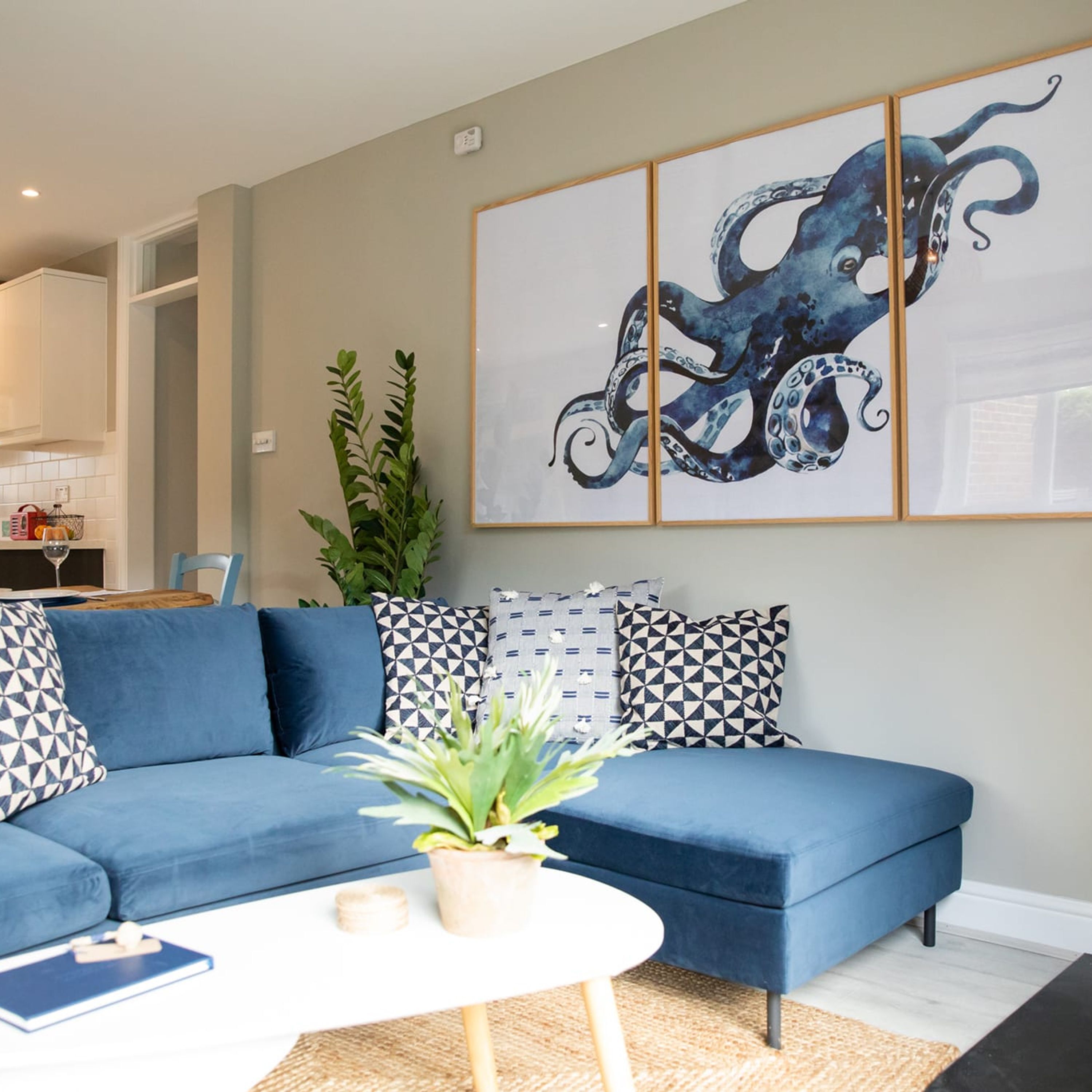 Ein modernes Wohnzimmer mit einem blauen Sofa, gemusterten Kissen, einem weißen Couchtisch und einem großen Octopus-Gemälde an der Wand.