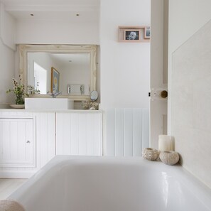 A bathroom with a bathtub, a mirror, a sink, and a framed picture on the wall. - Country Cottage in Pretty Village Quay Views (Chichester)