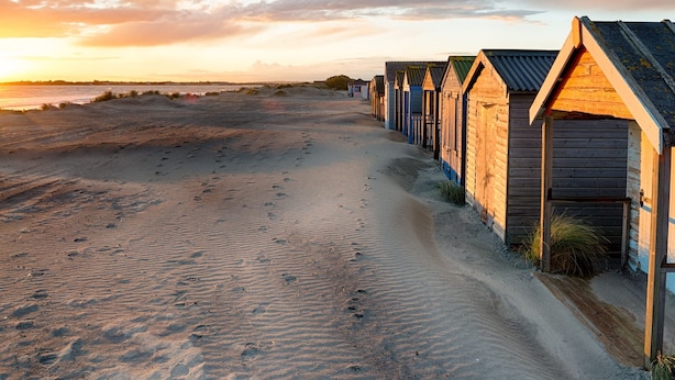 A row of wooden beach huts along a sandy path with footprints leading to the beach. - Sunny Modern Nr Beach Village w Parking (Chichester)