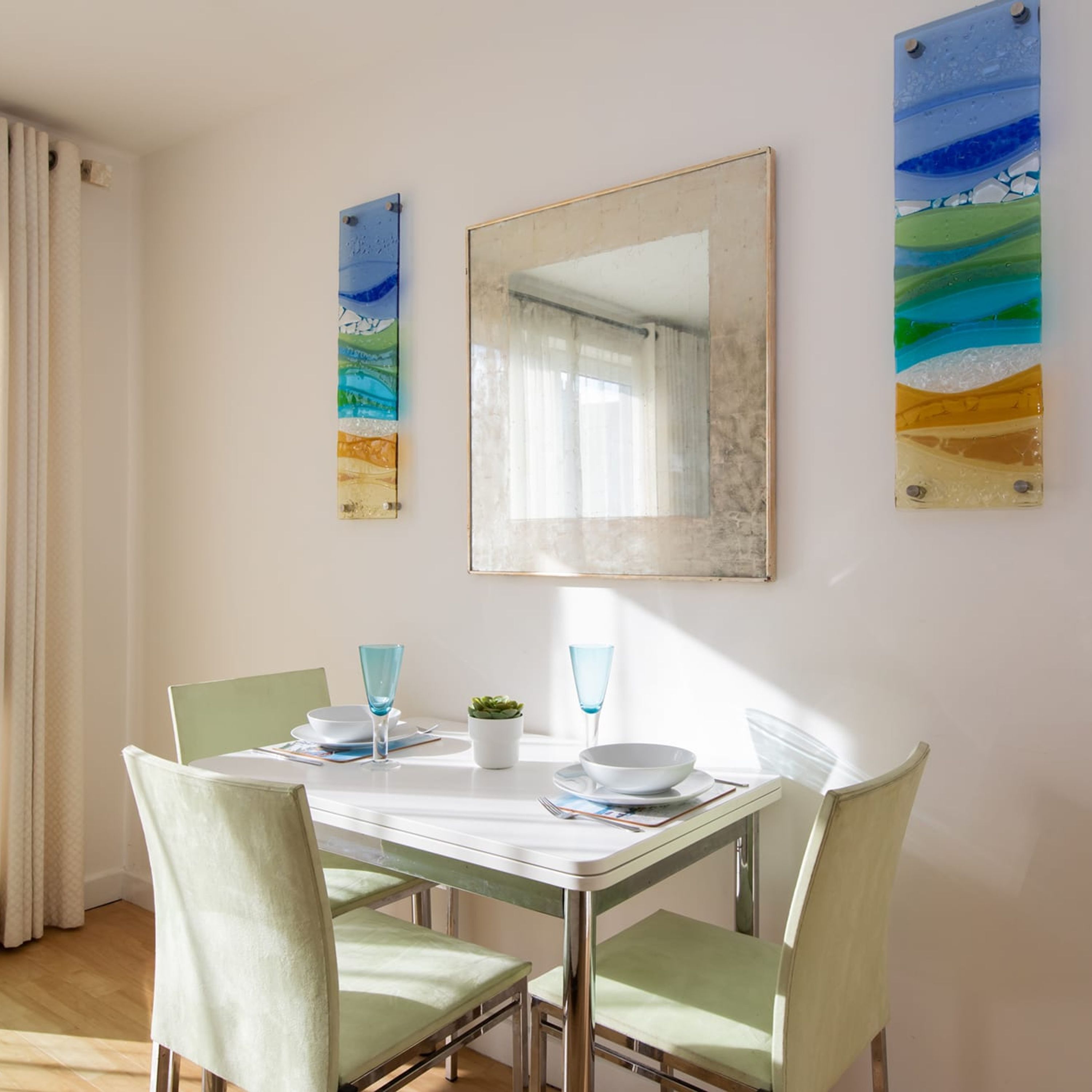 A dining area with a table set for two, two chairs, a potted plant, and two blue glassware items.
