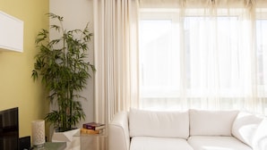A modern living room with a white sofa, a large bamboo plant, and a flat-screen TV on a glass table. - Sunny Modern Nr Beach Village w Parking (Chichester)