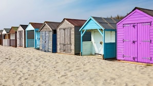 A row of beach huts with varying colors and simple designs, lined up along a sandy beach. - Sunny Modern Nr Beach Village w Parking (Chichester)