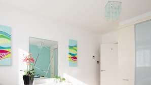 A modern bedroom with a large bed, white walls, and a large mirror. There are two blue towels on the bed and a potted plant on the dresser. - Sunny Modern Nr Beach Village w Parking (Chichester)