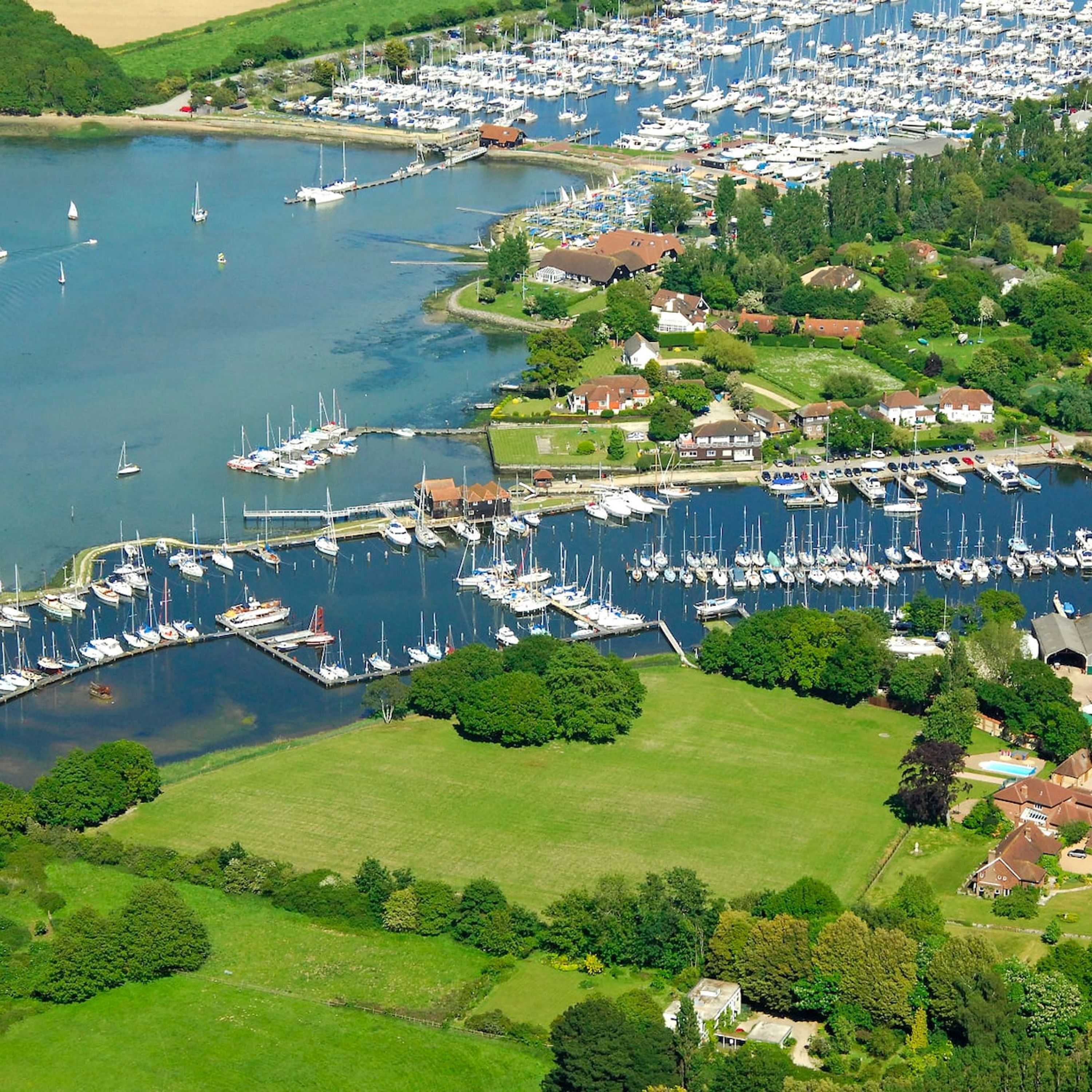 Luchtbeeld van een jachthaven met vele boten afgemeerd, omringd door weelderige begroeiing en woongebouwen.
