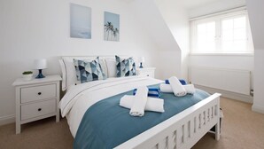 A bedroom with a bed, nightstands, a lamp, and artwork on the wall. - Modern Stylish Seaside Family Home (Chichester)