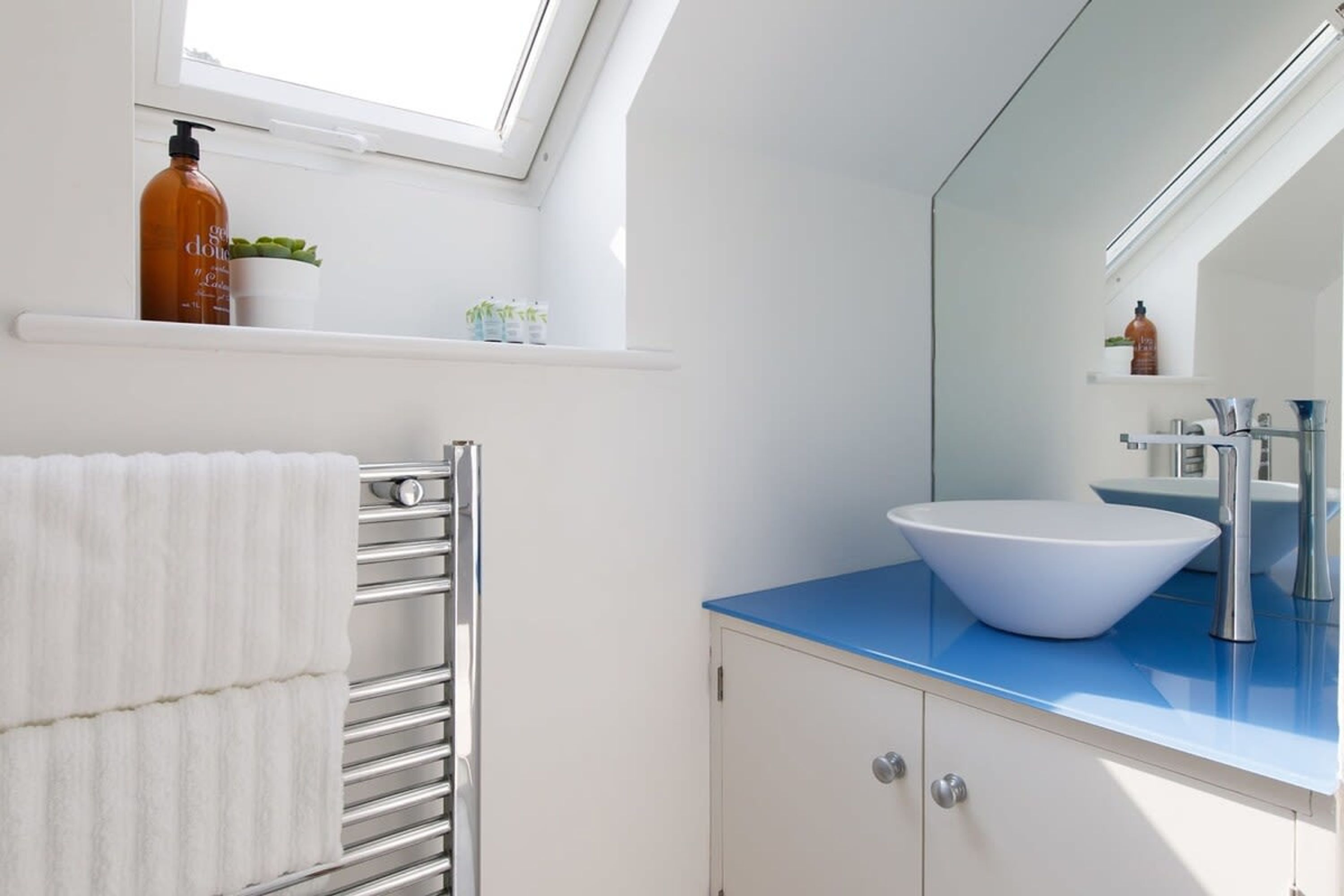 A modern bathroom with a skylight, white walls, a blue countertop, a white sink, and a towel rack.