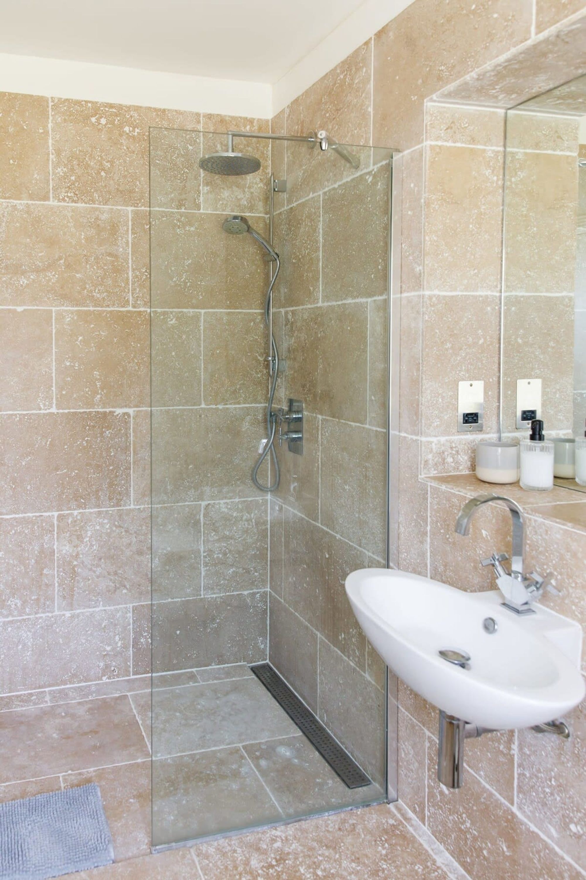 A modern bathroom with a glass-enclosed shower, a white sink, and beige tiled walls.